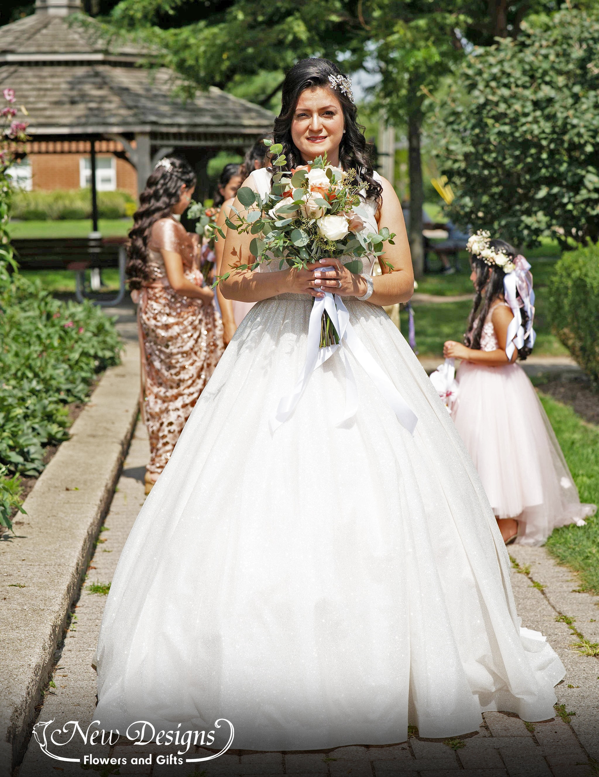 A bride stands holding her bouquet of full roses in white, nude and orangey pink roses